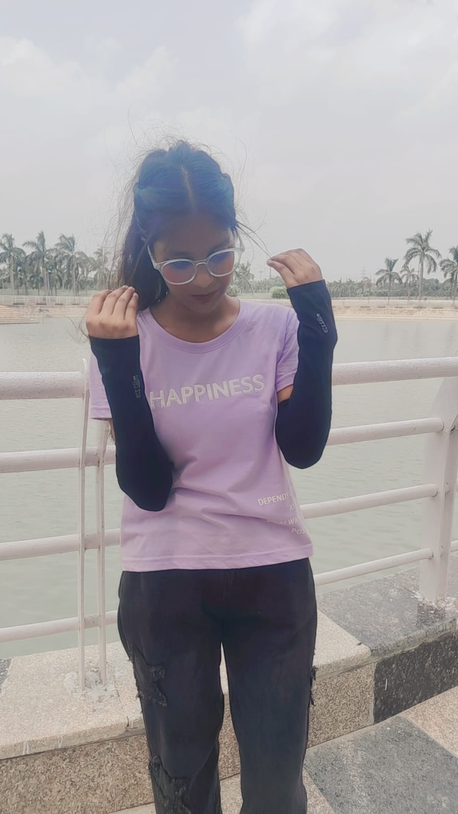 Saumya in a lavender ‘Happiness’ T-shirt and clear glasses by the lake, smiling down