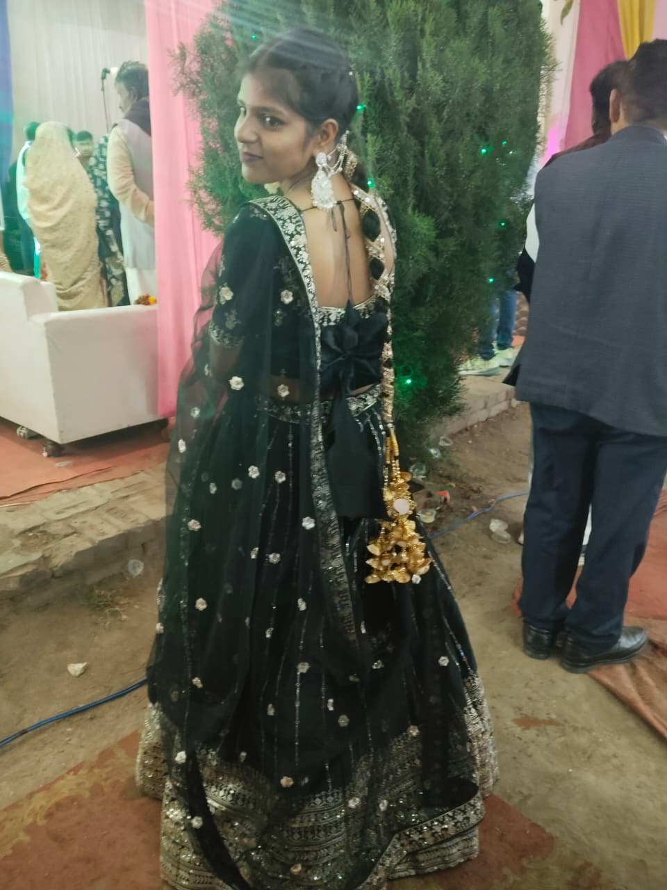 Saumya in a black embroidered lehenga, glancing back over one shoulder at a wedding
