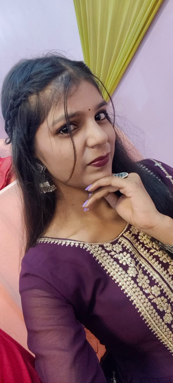 Close-up selfie of Saumya in a plum suit with gold embroidery, chin resting on one hand