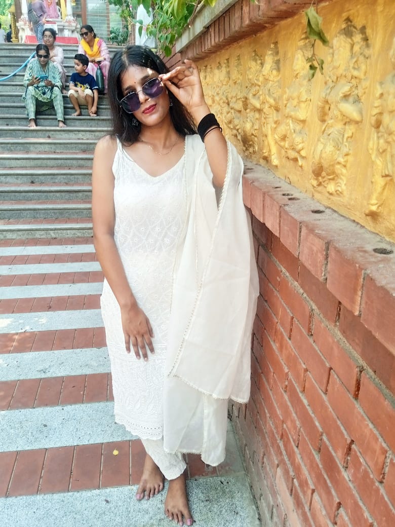 Saumya in a white chikankari suit and sunglasses beside a golden carved temple wall