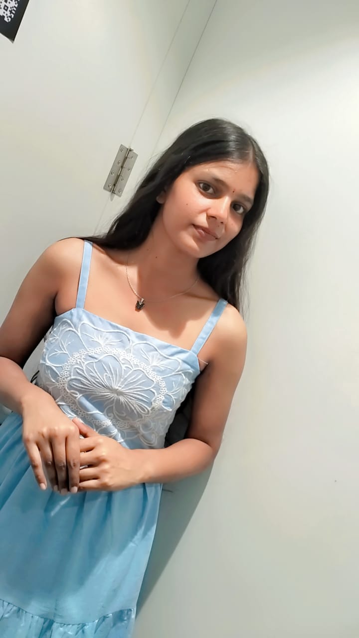 Saumya in a pale-blue embroidered sundress, leaning against a white wall